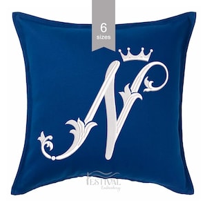 May include: A square, navy blue pillow with a white embroidered letter "N" and a crown. The letter is stylized with decorative flourishes. The text "6 sizes" is in a gray rectangle at the top. The text "FESTIVAL Embroidery" is at the bottom.