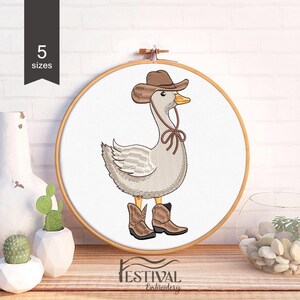 Könnte beinhalten: Stickdatei einer Gans, die einen braunen Cowboyhut und Stiefel trägt. Die Gans steht auf einem weißen Hintergrund.