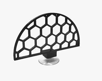 Puede incluir: Objeto decorativo negro semicircular con un patrón de panal. El objeto está montado sobre una pequeña base cuadrada y una ventosa circular transparente. El diseño es moderno y geométrico.