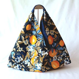 Op de afbeelding: Een blauwe tote bag met een citroen- en bloemenprint. De tas is gemaakt van stof en heeft een driehoekige vorm.