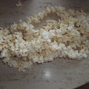 May include: A large pile of white popcorn on a light brown surface.