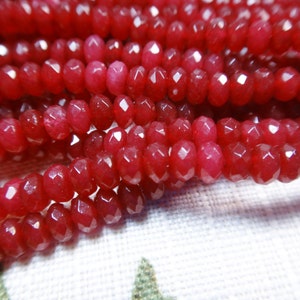 Op de afbeelding: Een streng rode gefacetteerde edelsteen kralen. De kralen zijn rond en hebben een gladde, gepolijste afwerking.