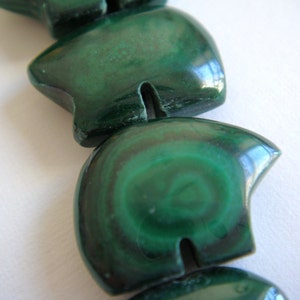 May include: A close-up of a green malachite bead necklace. The beads are carved into a heart shape and have a smooth, polished finish.