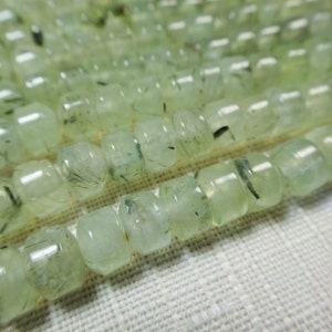 May include: A strand of light green gemstone beads with black inclusions. The beads are round and have a smooth, polished finish.