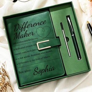 May include: A dark green notebook set in a matching box, featuring the text Difference Maker with a heart outline, a definition, and the name Sophia. The set includes a notebook with a gold-toned clasp, a black pen, and a silver-toned pen refill.