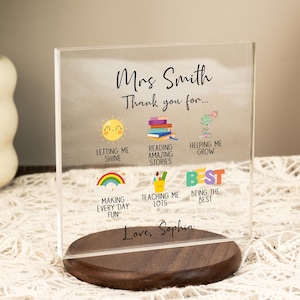 Può includere: Un blocco di acrilico trasparente con il testo "Mrs. Smith Thank you for..." e icone colorate. Il blocco poggia su una base di legno scuro. Il testo include "Letting Me Shine", "Reading Amazing Stories" e "Helping Me Grow".