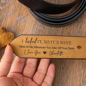 以下が含まれることがあります： 黒い革のベルトで、端にパーソナライズされたメッセージが書かれています。メッセージは「私が手に入れたので、それは私のものです。ズボンを脱ぐときはいつでも私のことを考えてください。愛してる、シャーロット」と書かれています。