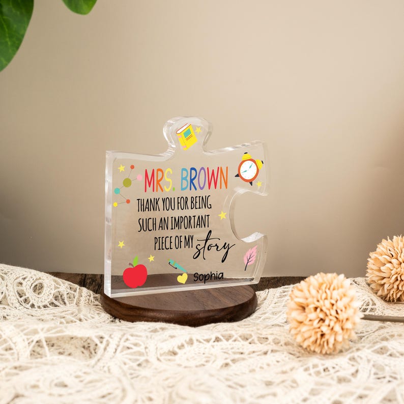 May include: A clear acrylic puzzle piece with the text "MRS. BROWN THANK YOU FOR BEING SUCH AN IMPORTANT PIECE OF MY story Sophia". The puzzle piece is on a dark wooden base, with colorful graphics and a clock.