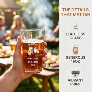 May include: A clear 16 oz glass featuring a printed graphic of a hand holding a beer and another hand holding a baby bottle. The text reads Our first CHRISTMAS TOGETHER, Tina & Daddy CHEERS! 2025. The side panel lists features: LEAD-LESS GLASS, 16OZ, VIBRANT PRINT.