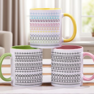 Puede incluir: Tres tazas de cerámica blanca con diseños coloridos. Una taza tiene un asa y un interior amarillos, otra tiene un asa y un interior verdes, y la tercera tiene un asa y un interior rosas. Cada taza presenta un patrón diferente de líneas negras y coloridas.