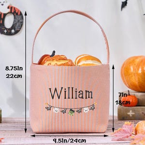 Puede incluir: Un bolso tote con tem&aacute;tica de Halloween, de 22 cm de alto y 24 cm de ancho, con un dise&ntilde;o a rayas rojas y blancas. La bolsa presenta el nombre "William" y una pancarta con iconos de Halloween. Contiene calabazas decorativas.