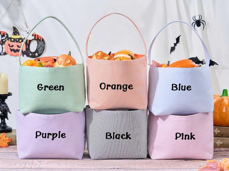 Puede incluir: Seis coloridas bolsas de golosinas de Halloween de tela seersucker en verde, naranja, azul, morado, negro y rosa. Cada bolsa est&aacute; llena de calabazas decorativas. Las bolsas tienen un asa y el nombre del color est&aacute; impreso.