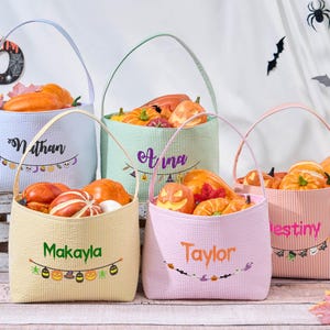 Puede incluir: Cinco cestas de Halloween de colores pastel llenas de calabazas y calabacines. Cada cesta tiene un nombre bordado en la parte delantera. Las cestas tienen un patr&oacute;n de rayas o cuadros y un asa. Los colores son pastel.
