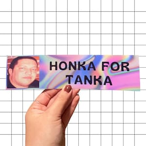 May include: A rectangular sticker with the text "HONKA FOR TANKA" in black capital letters. The sticker has a holographic background with pink, blue, and purple hues. A photo of a man is on the left side of the sticker.