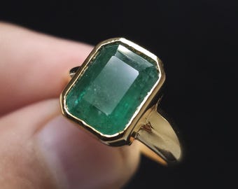 May include: A gold ring with a large, emerald green gemstone. The gemstone is cut in a rectangular shape with beveled edges.