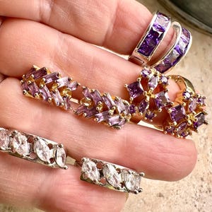 May include: A collection of rings featuring various designs, including bands with channel-set deep purple rectangular stones, clusters of purple stones in gold settings, and bands with clear marquise-cut stones in silver-toned metal settings.