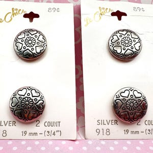 May include: Two cards of silver-colored buttons with heart and flower designs. Each button is 3/4 inch (19 mm) in diameter. The cards are labeled "Le Chic" and "Silver 918".