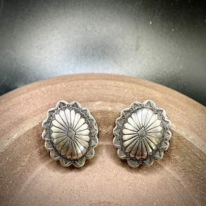 May include: A pair of silver earrings with a geometric design. The earrings are oval shaped and have a raised, textured center.