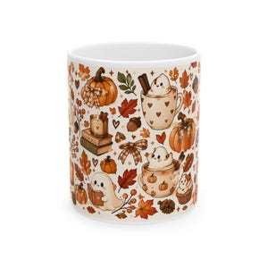 Puede incluir: Una taza de cerámica blanca con un patrón repetitivo de ilustraciones con temática otoñal que incluye calabazas naranjas, bellotas marrones, hojas de otoño coloridas, lazos a cuadros, pilas de libros, velas y pequeños fantasmas en tazas.