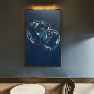 Peut inclure: Une peinture encadrée de deux bulles colorées qui se chevauchent sur un fond bleu foncé. La peinture est accrochée au mur au-dessus d'une petite table ronde et d'une chaise en bois.