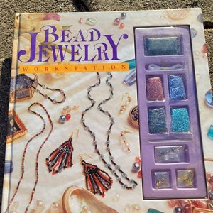 May include: A Bead Jewelry Workstation kit with a purple tray containing beads, string, and tools. The cover of the book features a colorful beaded necklace and earrings.