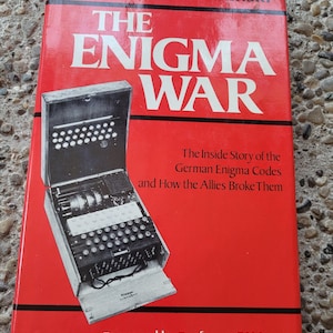 May include: A red hardcover book titled "The Enigma War" by Józef Garliński. The book cover features a black and white image of an Enigma machine, a German cipher device used during World War II. The text on the cover reads "The Inside Story of the German Enigma Codes and How the Allies Broke Them." The book also includes a foreword by Professor R.V. Jones.