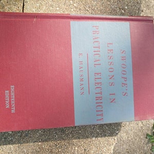 Könnte beinhalten: Ein rotes Hardcover-Buch mit dem Titel "Swoope's Lessons in Practical Electricity" von E. Hausmann. Das Buch ist die achtzehnte Auflage.