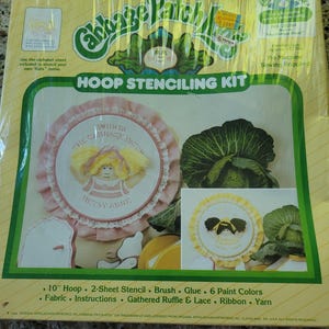 May include: A Cabbage Patch Kids Hoop Stenciling Kit in yellow packaging. The kit includes a 10-inch hoop, two stencil sheets, a brush, glue, six paint colors, fabric, instructions, gathered ruffle, lace, ribbon, and yarn for crafting projects.