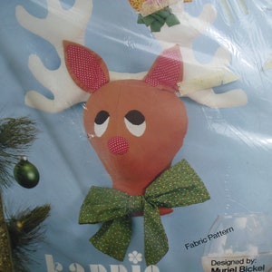 May include: A vintage fabric pattern for a reindeer head with a green and white polka dot bow. The pattern is called "KAPPIO" and is designed by Muriel Bickel. The pattern is labeled as a "Fabric Pattern".