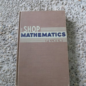 Puede incluir: Un libro antiguo titulado "SHOP MATHEMATICS" de Felker. La portada es de color marrón apagado con el título en letras azules en negrita y líneas horizontales blancas. El libro parece estar en buen estado.