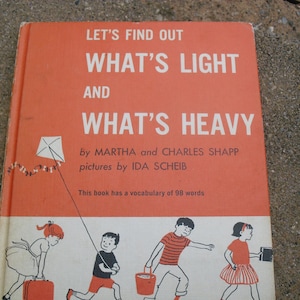 Puede incluir: Una portada de libro infantil vintage con fondo rojo y el título "Let's Find Out What's Light and What's Heavy" de Martha y Charles Shapp. La portada presenta ilustraciones de niños sosteniendo varios objetos.