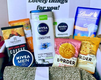May include: A gift box filled with various items, including Nivea Men skincare products, coffee, cookies, and a Lindt chocolate bar. The box also contains a green and beige sweater and a sign that reads "Lovely things for you!"