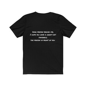 May include: Black t-shirt with white text: "DEAR PERSON BEHIND ME, I HOPE YOU HAVE A GREAT DAY! SINCERELY, THE PERSON IN FRONT OF YOU." The shirt is a casual wear item.