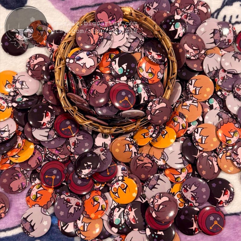 Pode incluir: Uma cole&ccedil;&atilde;o de bot&otilde;es de personagens de anime coloridos. Os bot&otilde;es est&atilde;o dispostos em uma cesta e espalhados sobre um tecido estampado roxo e branco. Os bot&otilde;es apresentam uma variedade de personagens com diferentes express&otilde;es e poses.