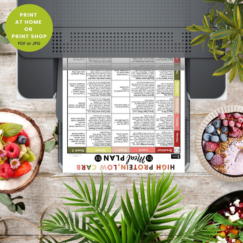 May include: A printed meal plan labeled "High Protein, Low Carb" is in a printer. The plan includes sections for breakfast, lunch, and dinner. The image also shows a bowl of fruit and a smoothie, with the text "Print at Home or Print Shop PDF or JPG".