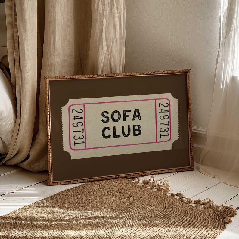 May include: A framed print featuring a ticket design with the words "SOFA CLUB" in black text. The ticket has a pink border and the number "249731" on each end. The frame is brown with a textured border.