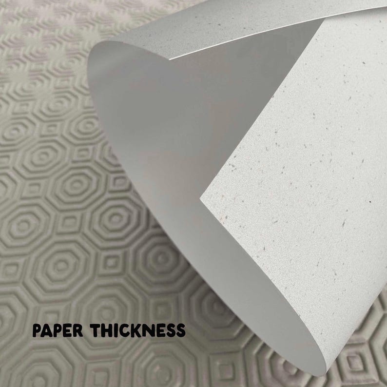 May include: Close-up of a rolled-up sheet of white paper with a speckled texture, revealing its thickness. The text "PAPER THICKNESS" is printed in black at the bottom. The background features a gray, patterned surface.