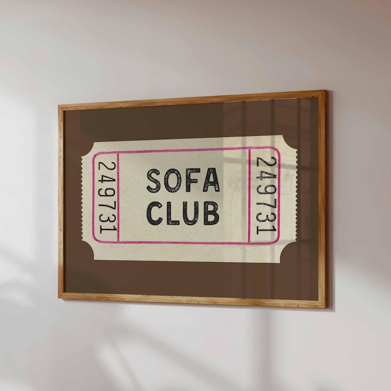 May include: A framed print featuring a vintage-style ticket design. The ticket has the words "SOFA CLUB" in bold black letters, with the number "249731" on each end. The frame is a warm brown color.