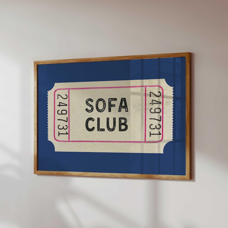 May include: A framed print featuring a vintage-style ticket design. The ticket has the words "SOFA CLUB" in a bold font, with the number "249731" on each side. The background is a deep blue, and the frame is a warm brown.