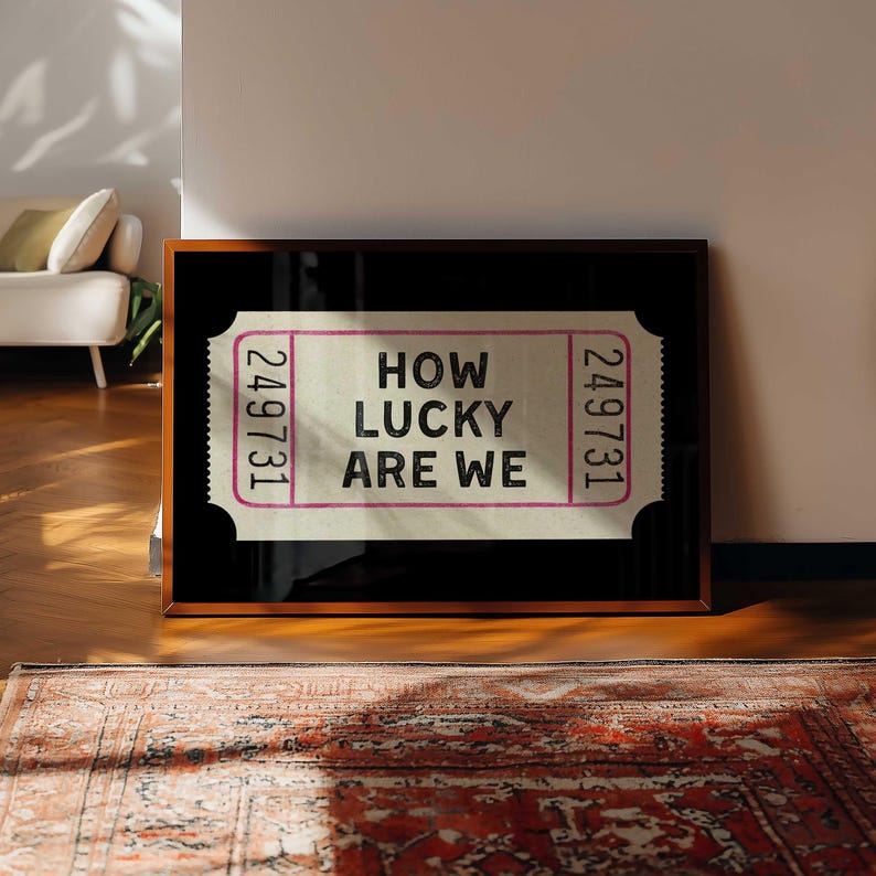 May include: A framed print featuring a ticket design with the text "HOW LUCKY ARE WE." The ticket has a light beige background with pink borders and the number "249731" on each end. The frame is dark brown.