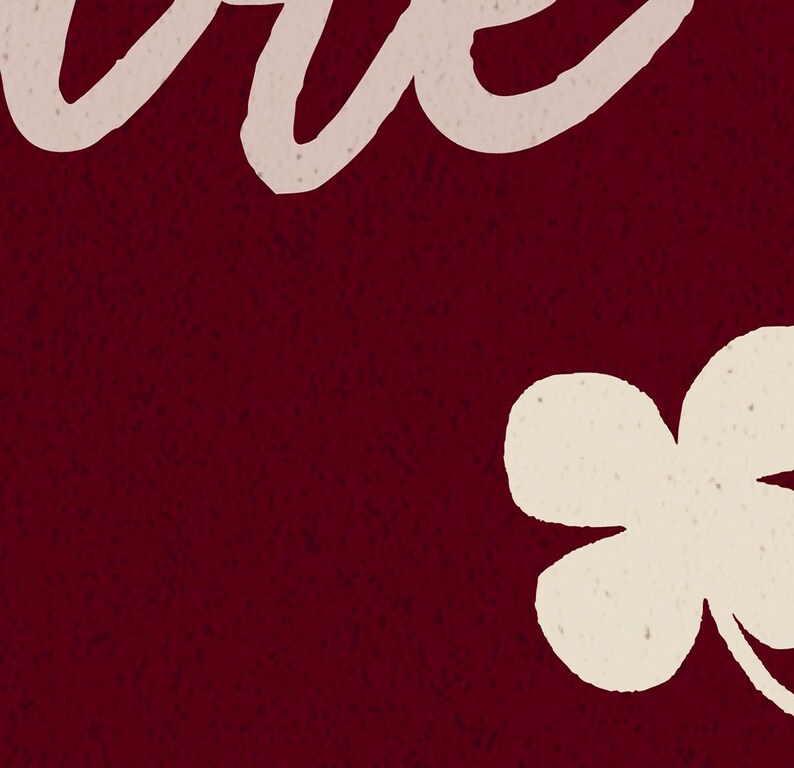 May include: A burgundy background with a textured appearance. The upper left corner features the word "love" in a cream-colored, cursive font. A cream-colored four-leaf clover is in the lower right corner.