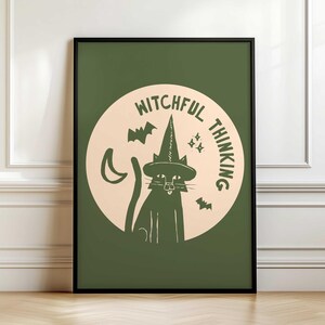 May include: A framed art print with a green background, featuring a black cat in a witch's hat. The cat is within a light beige circle, surrounded by bats, a crescent moon, stars, and the words "Witchful Thinking".
