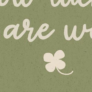 May include: A textured, olive green background with the words "how much are we" in a cream-colored, cursive font. A cream-colored four-leaf clover is at the bottom. The image has a vintage, rustic feel.