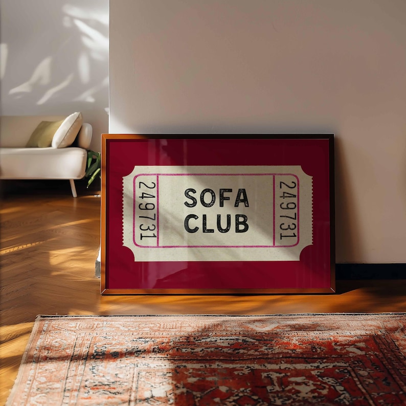 May include: A framed print featuring a ticket design with the words "SOFA CLUB" in black text. The ticket has a pink border and the number "249731" printed on each side. The frame is brown, and the background is a deep red.