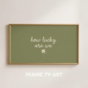 Puede incluir: Una impresión artística enmarcada con un marco dorado. La impresión tiene un fondo verde con las palabras "how lucky are we" en escritura blanca y un pequeño trébol blanco. Las palabras "FRAME TV ART" están en la parte inferior.