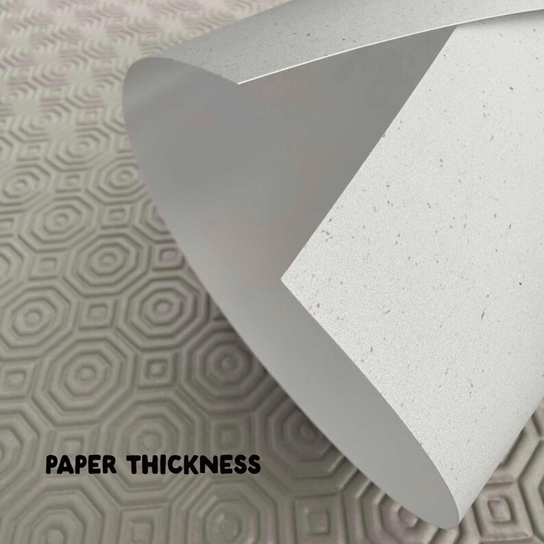 May include: Close-up of a rolled-up sheet of white paper with a speckled texture, revealing its thickness. The text "PAPER THICKNESS" is printed in black at the bottom. The background features a gray, patterned surface.