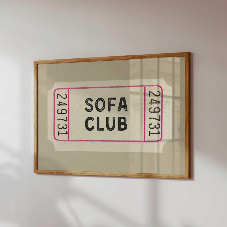 May include: A framed print featuring a vintage-style ticket design. The ticket has the words "SOFA CLUB" in black text, framed by a pink border, and the number "249731" on each end. The frame is made of light brown wood.