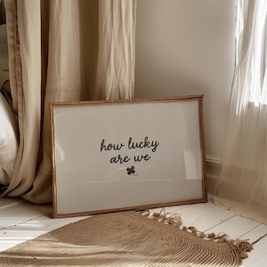 May include: A framed print with the words "how lucky are we" in black script, along with a small shamrock. The frame is a light brown color. A woven rug with fringe is in the foreground.