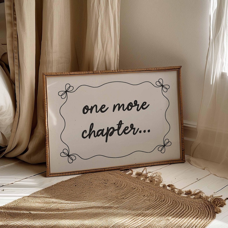 Printable bookish wall art featuring the words 'one more chapter...' in a handwritten style font with a wavy border and a bow in each corner. Black illustration on a beige background. Displayed in a large horizontal wooden frame in a neutral room.