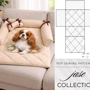 May include: A beige dog bed featuring a Cavalier King Charles Spaniel print. The bed has a quilted design and is framed by bolster pillows and a bone-shaped pillow, all adorned with brown bows. The bed is placed on a grey sofa.